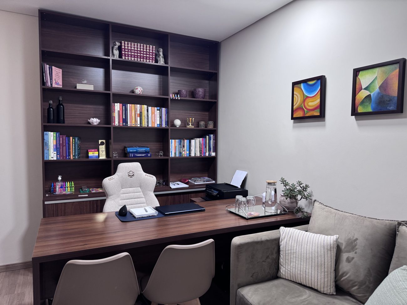 Sala de atendimento com estante de livros, mesa de madeira e sofá