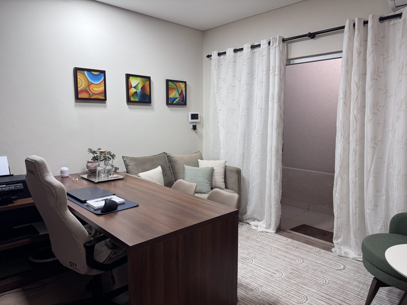 Ambiente do consultório com sofá, quadros coloridos e cortinas claras